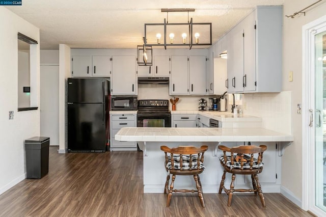 kitchen with pendant lighting, black appliances, decorative backsplash, dark hardwood / wood-style flooring, and kitchen peninsula