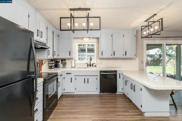 kitchen featuring black appliances, a healthy amount of sunlight, kitchen peninsula, and hanging light fixtures