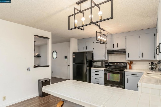 kitchen with tile counters, tasteful backsplash, dark hardwood / wood-style floors, pendant lighting, and black appliances