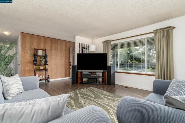 living room with a textured ceiling, dark wood-type flooring, and wooden walls