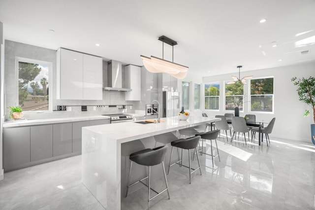 kitchen with white cabinets, wall chimney exhaust hood, stainless steel electric range, and decorative light fixtures