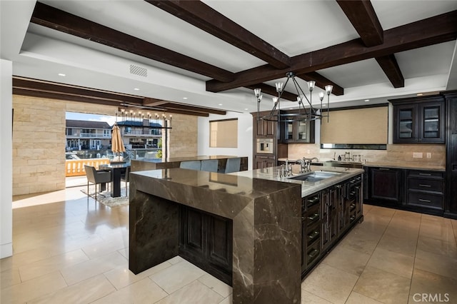 kitchen with a large island with sink, tasteful backsplash, beam ceiling, and sink