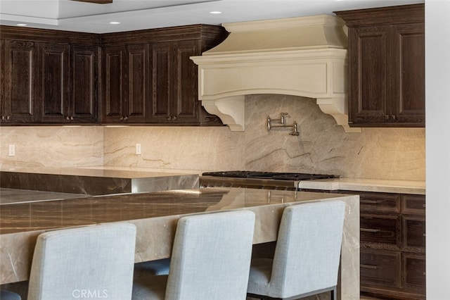 kitchen featuring dark brown cabinetry, decorative backsplash, custom range hood, and stainless steel range oven