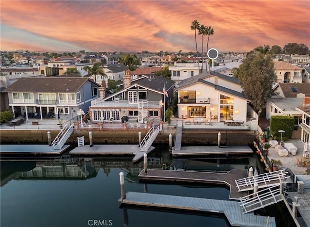 back house at dusk featuring a water view and a balcony