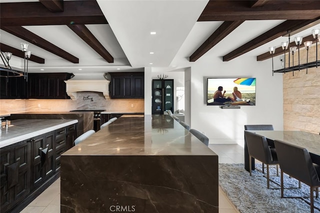 kitchen featuring beamed ceiling, a large island, light stone counters, and backsplash