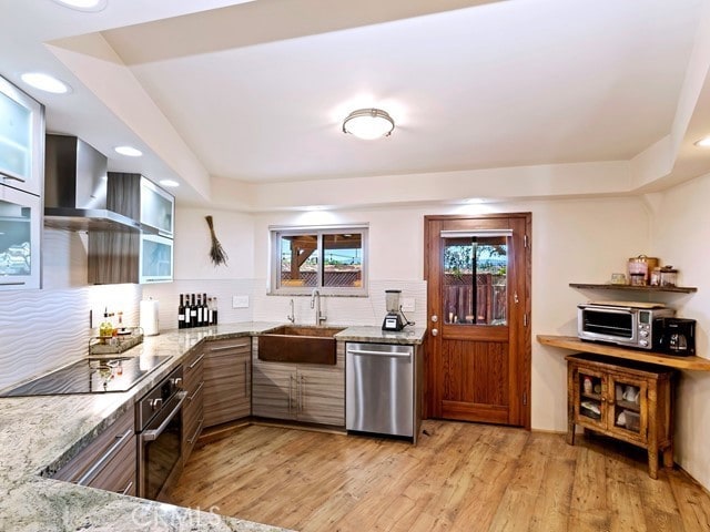 kitchen with sink, light wood-type flooring, stainless steel appliances, wall chimney exhaust hood, and light stone counters