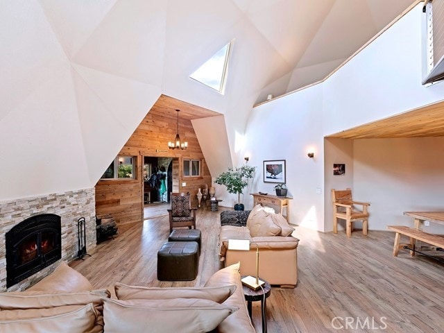 living room with a stone fireplace, high vaulted ceiling, wood walls, light hardwood / wood-style floors, and a notable chandelier