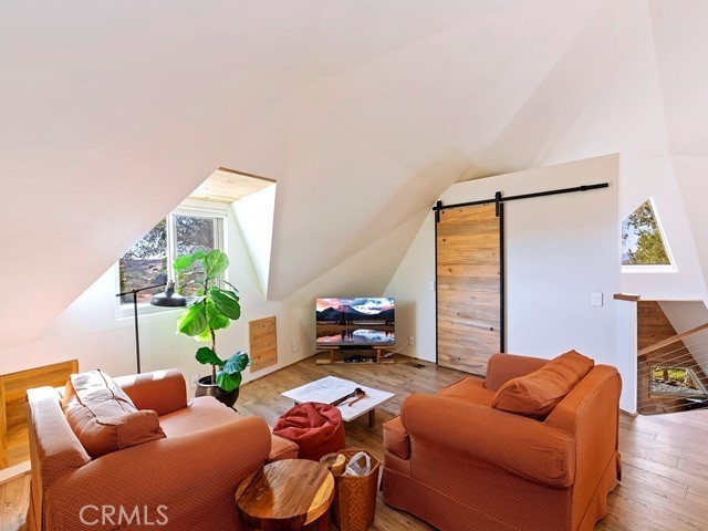 living room with a barn door, light wood-type flooring, and vaulted ceiling