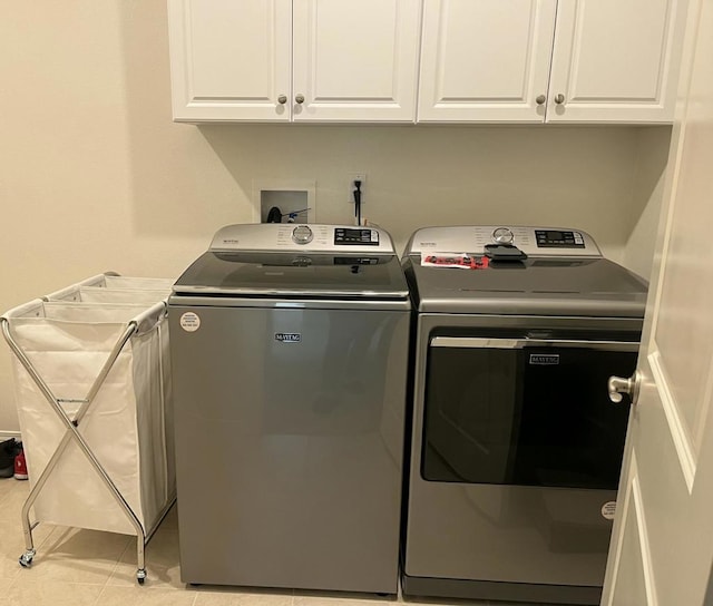 laundry area with washing machine and dryer, light tile patterned floors, and cabinets