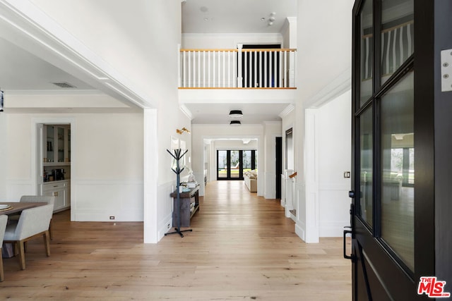 foyer with a high ceiling, light wood-type flooring, french doors, and ornamental molding