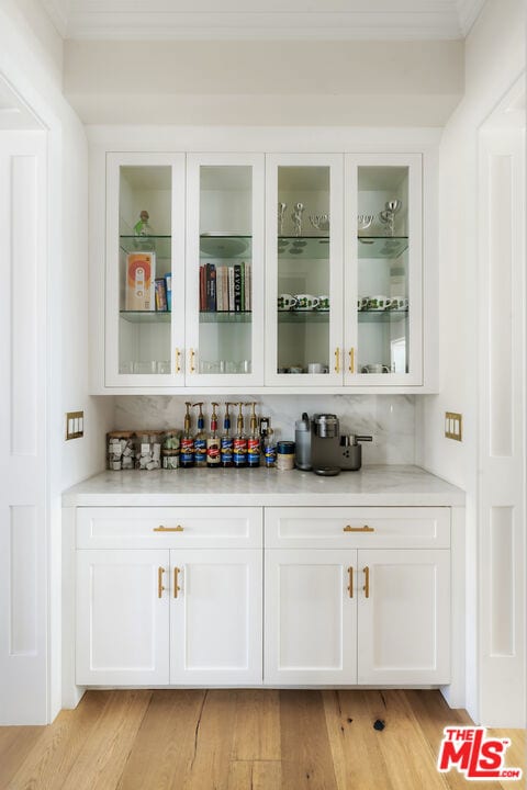 bar with white cabinets and light wood-type flooring