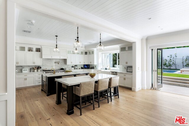 kitchen featuring white cabinetry, a center island with sink, hanging light fixtures, and light hardwood / wood-style flooring