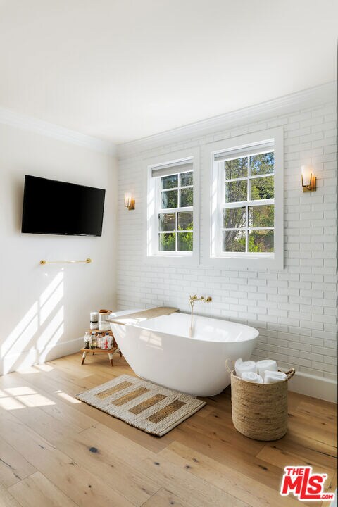 bathroom with hardwood / wood-style floors, a bathtub, crown molding, and brick wall