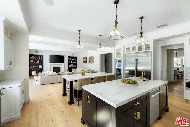 kitchen with light wood-type flooring, a center island with sink, stainless steel built in fridge, and white cabinetry