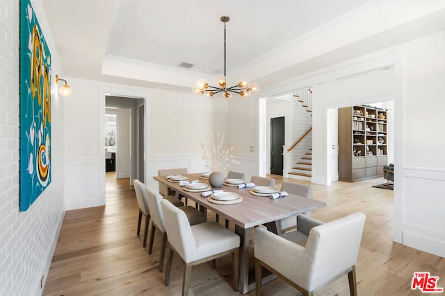 dining space featuring a raised ceiling, crown molding, light hardwood / wood-style floors, brick wall, and a chandelier