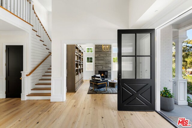 entryway with a tile fireplace, a towering ceiling, light wood-type flooring, wooden walls, and ornamental molding