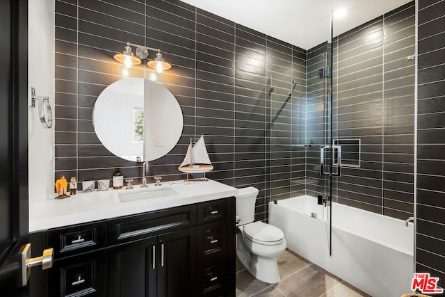 full bathroom featuring tile patterned flooring, toilet, shower / bath combination with glass door, vanity, and tile walls