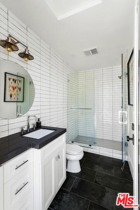 bathroom with vanity, backsplash, tile patterned floors, toilet, and tile walls