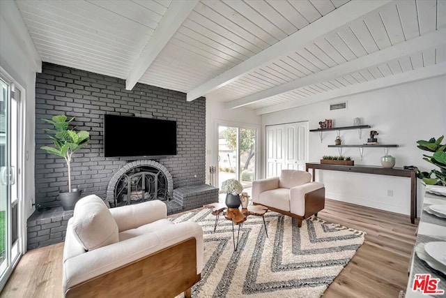 living room featuring beam ceiling, light hardwood / wood-style floors, and a brick fireplace