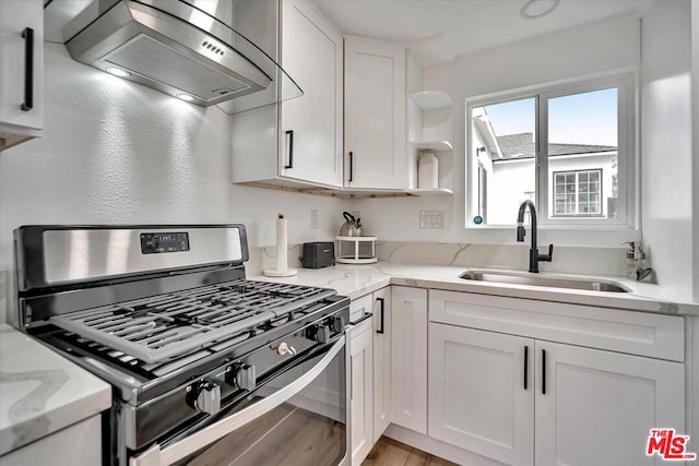 kitchen featuring stainless steel gas stove, white cabinets, wall chimney range hood, and sink