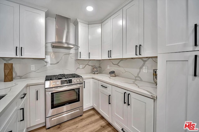 kitchen with wall chimney range hood, light wood-type flooring, gas stove, light stone counters, and white cabinetry