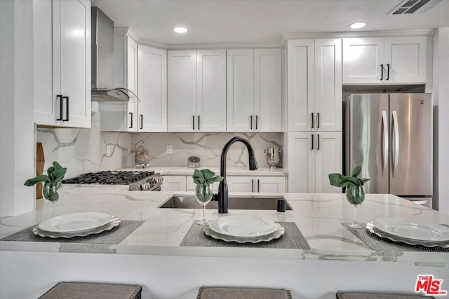 kitchen featuring stainless steel appliances, light stone counters, white cabinetry, and wall chimney exhaust hood