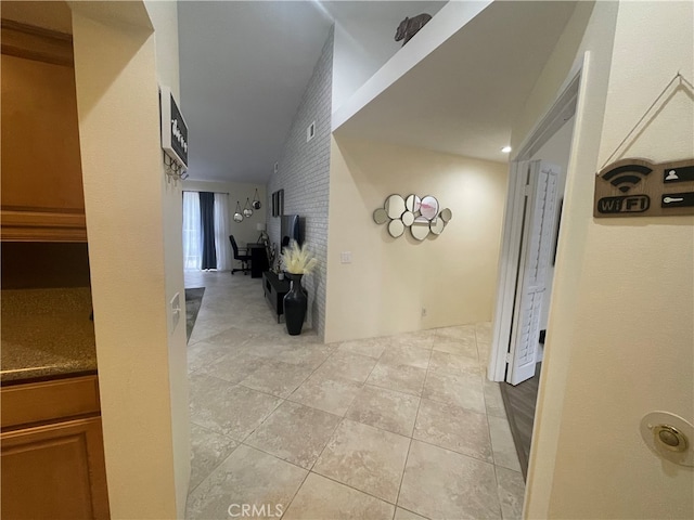 hall featuring light tile patterned floors, brick wall, and vaulted ceiling