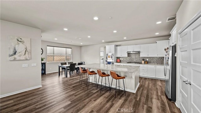 kitchen featuring a kitchen bar, stainless steel appliances, a kitchen island with sink, light stone countertops, and white cabinets