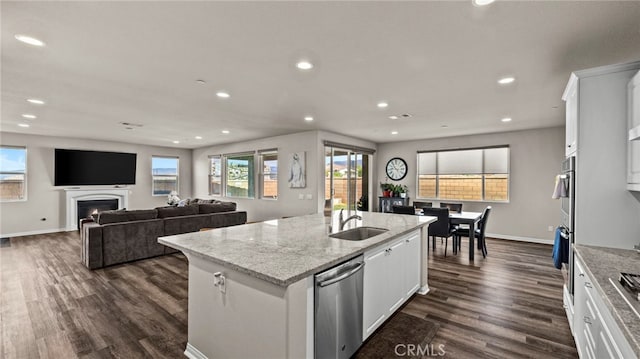 kitchen with white cabinetry, stainless steel appliances, an island with sink, sink, and light stone counters