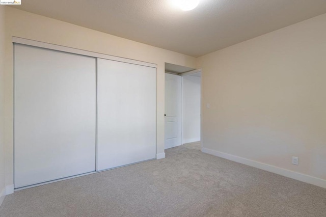 unfurnished bedroom with light colored carpet and a closet