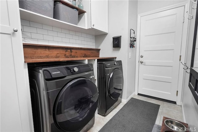 clothes washing area with washing machine and dryer, light tile patterned flooring, and cabinets