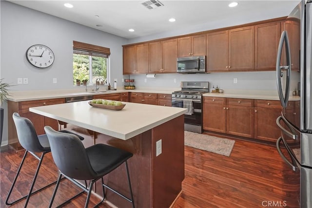 kitchen with appliances with stainless steel finishes, a breakfast bar, dark wood-type flooring, sink, and a kitchen island