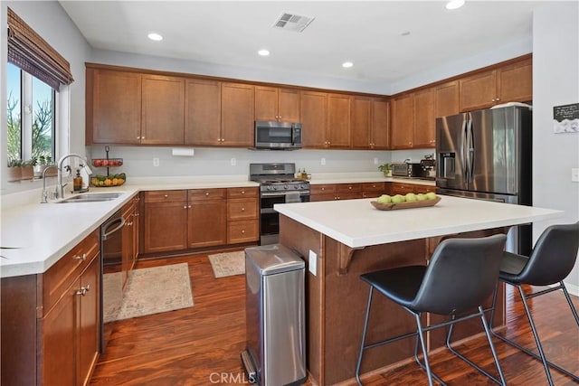 kitchen featuring a center island, dark wood-type flooring, sink, appliances with stainless steel finishes, and a kitchen bar