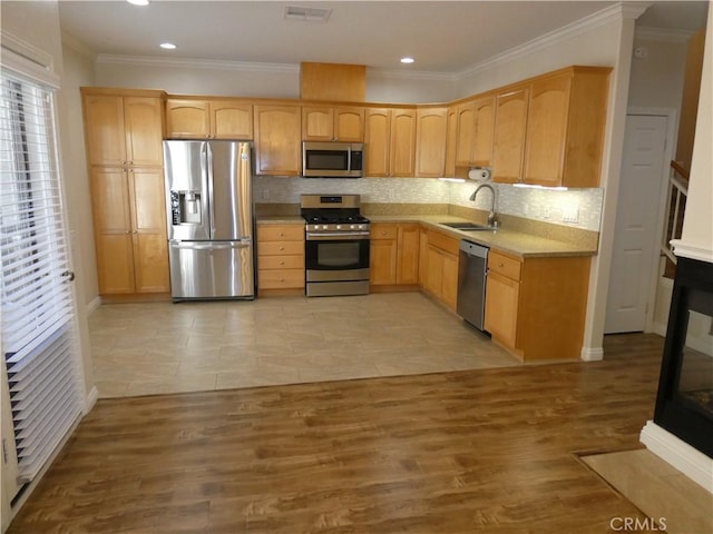 kitchen with light brown cabinetry, ornamental molding, stainless steel appliances, sink, and light hardwood / wood-style floors