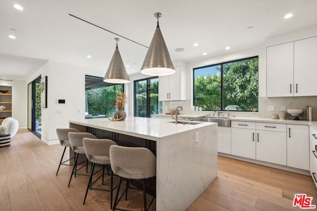 kitchen featuring white cabinetry, a kitchen island with sink, pendant lighting, and light wood-type flooring