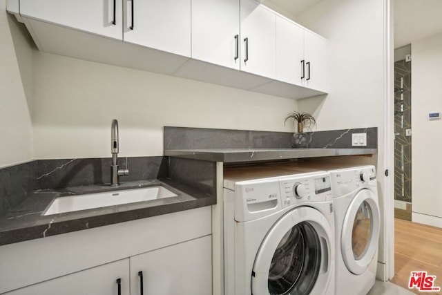 clothes washing area with light hardwood / wood-style floors, cabinets, separate washer and dryer, and sink