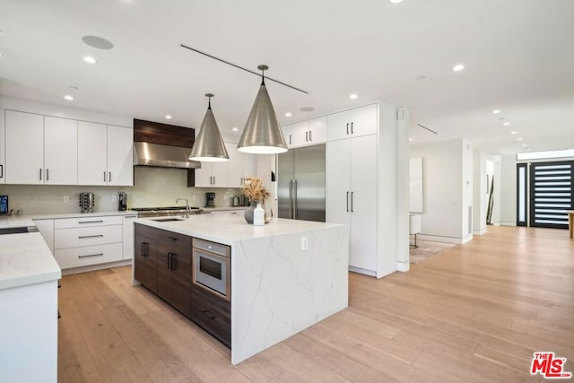 kitchen with a kitchen island with sink, pendant lighting, wall chimney range hood, and light hardwood / wood-style floors