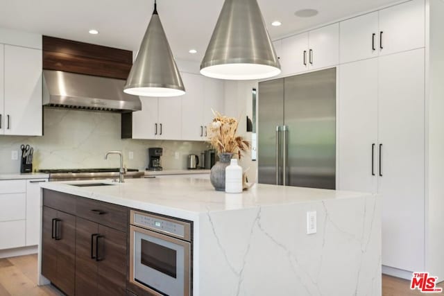 kitchen with a center island with sink, ventilation hood, light hardwood / wood-style flooring, decorative backsplash, and stainless steel appliances