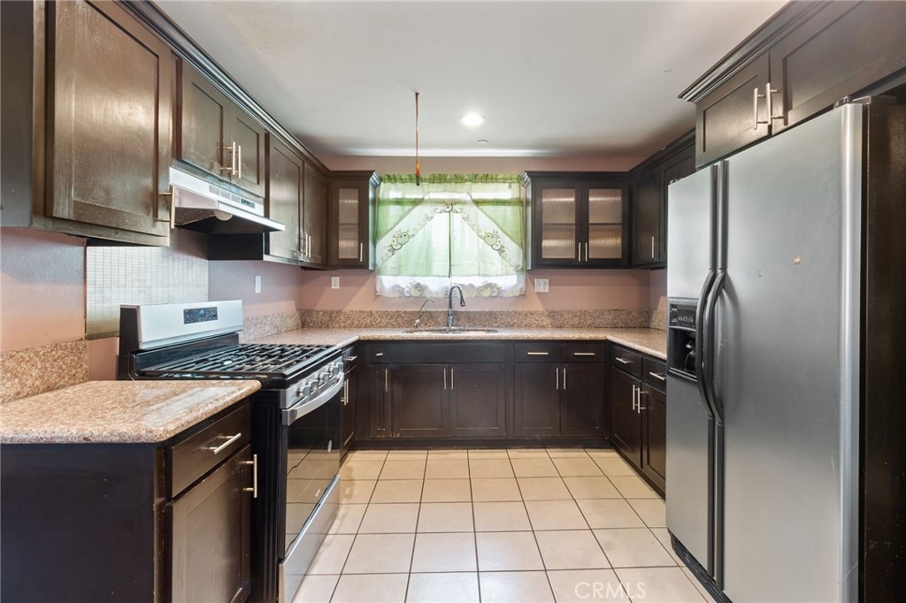 kitchen with sink, gas range, stainless steel fridge with ice dispenser, light tile patterned flooring, and dark brown cabinetry