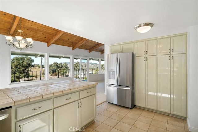 kitchen featuring a wealth of natural light, stainless steel fridge, cream cabinets, and tile countertops