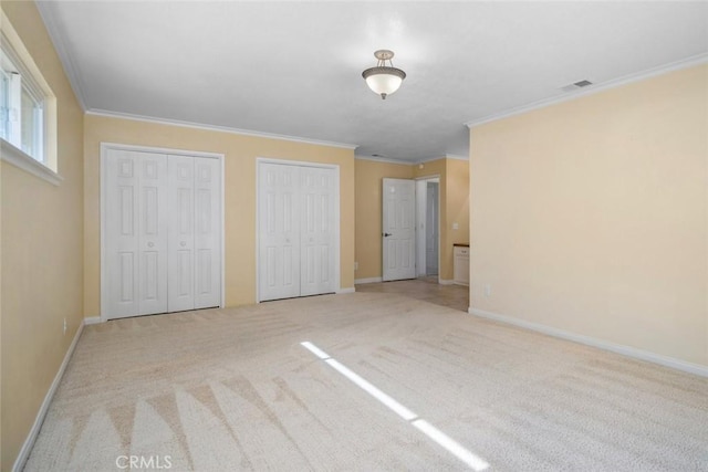 unfurnished bedroom featuring light colored carpet, crown molding, and two closets