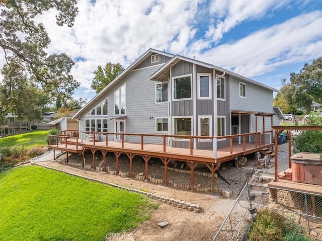 rear view of property with a lawn, board and batten siding, a hot tub, and a wooden deck