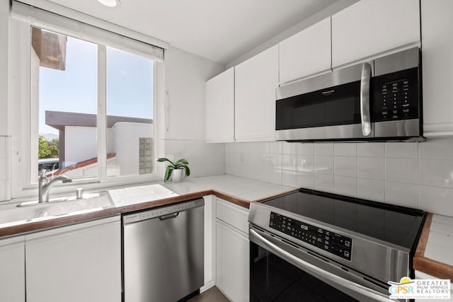 kitchen featuring a wealth of natural light, white cabinetry, stainless steel appliances, decorative backsplash, and sink