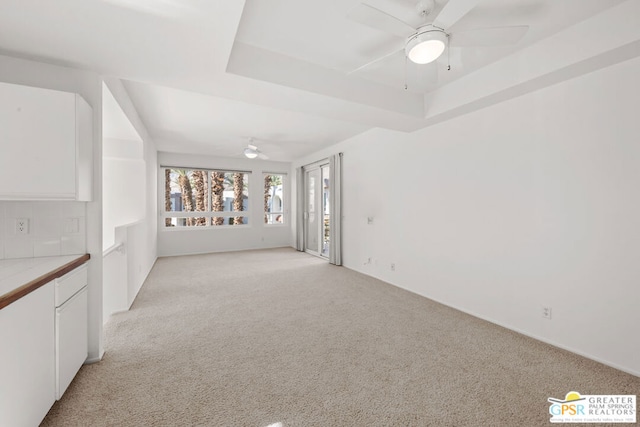 empty room with light carpet, ceiling fan, and a raised ceiling