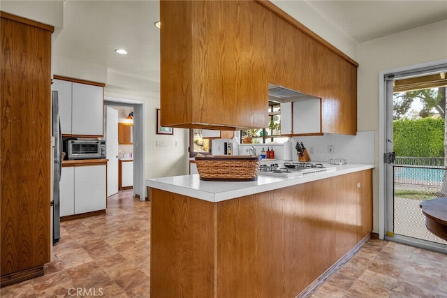 kitchen featuring white gas stovetop, backsplash, kitchen peninsula, white cabinetry, and stainless steel refrigerator