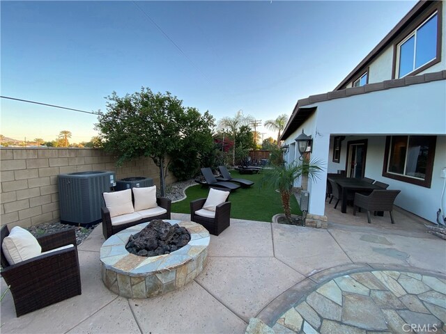 patio terrace at dusk featuring central AC and an outdoor living space with a fire pit