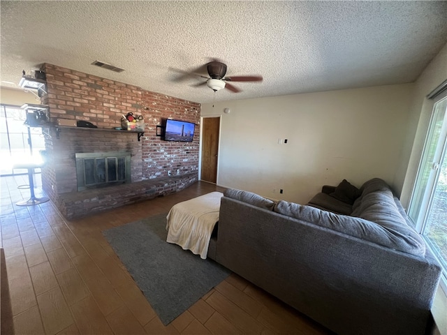 living room featuring a textured ceiling, a brick fireplace, dark hardwood / wood-style floors, and ceiling fan