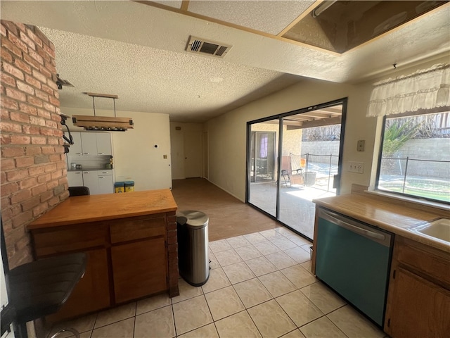 kitchen featuring stainless steel dishwasher, wood counters, a textured ceiling, and light tile patterned floors