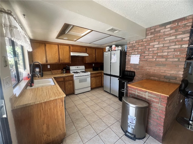 kitchen with light tile patterned flooring, white range with gas stovetop, brick wall, decorative backsplash, and stainless steel refrigerator