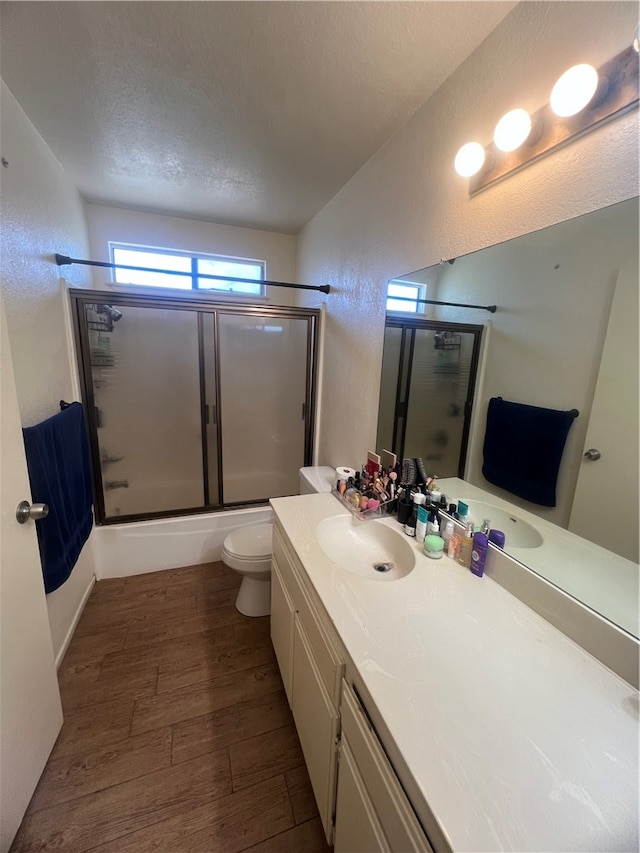 full bathroom with hardwood / wood-style floors, combined bath / shower with glass door, a textured ceiling, toilet, and vanity